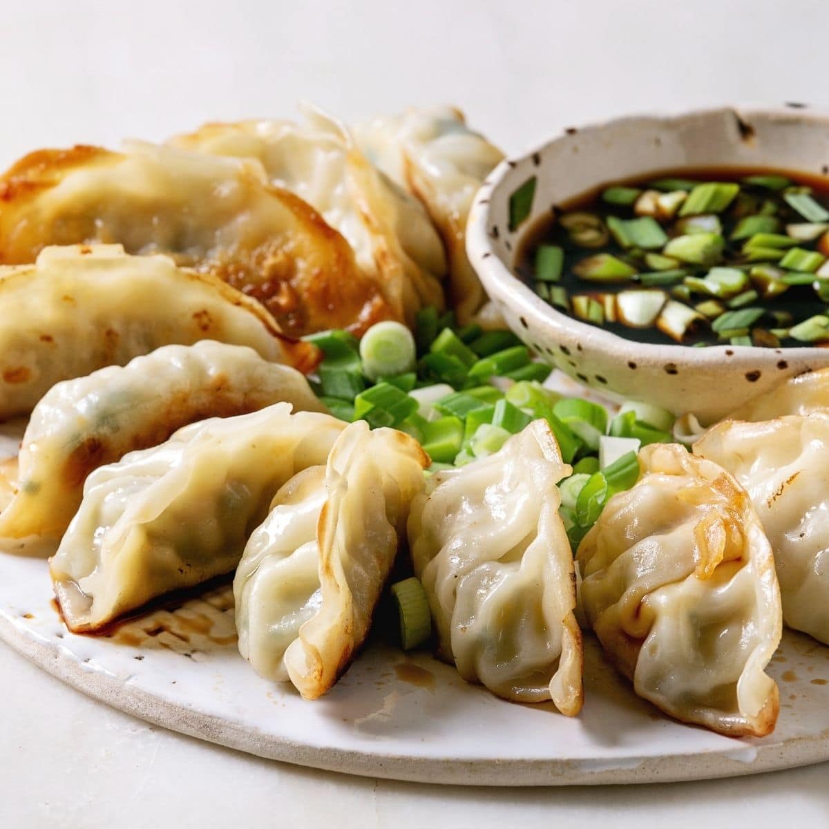 Square image of potstickers with a dipping sauce.