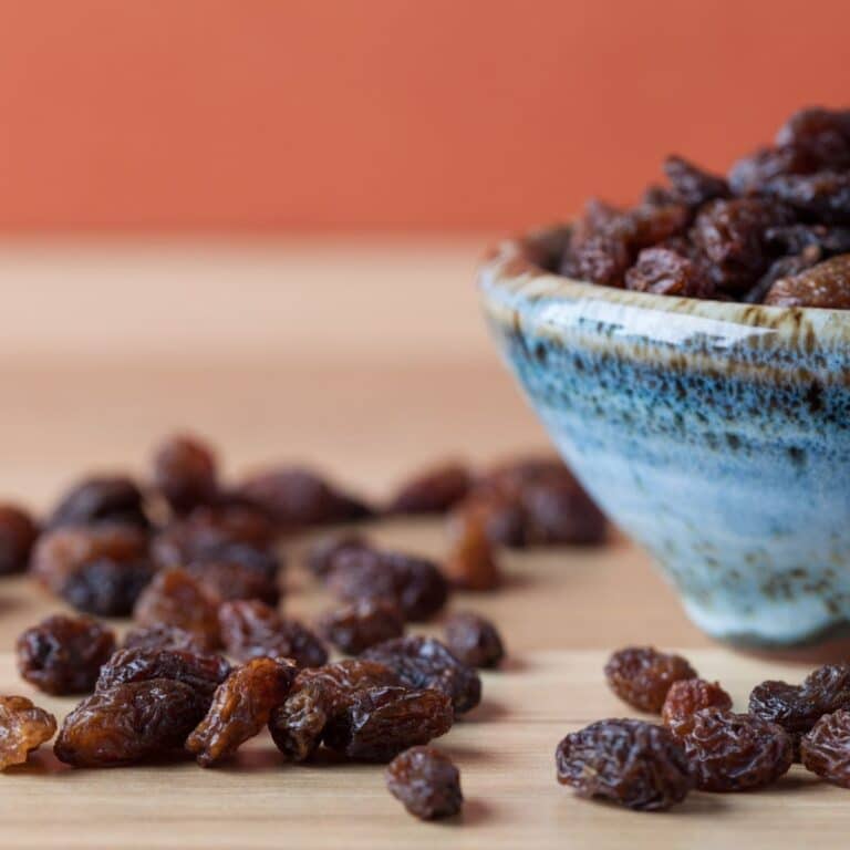 Square image of raisins on a table and in a bowl.