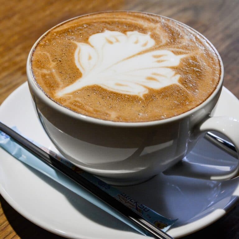 Square image of a latte in a white mug on a coaster.