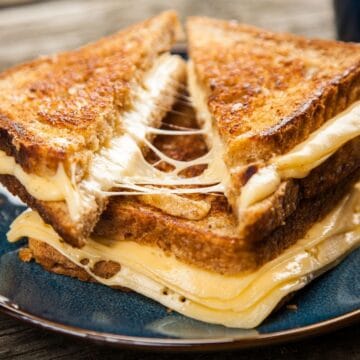 Square image of 2 grilled cheese sandwiches on a blue plate.