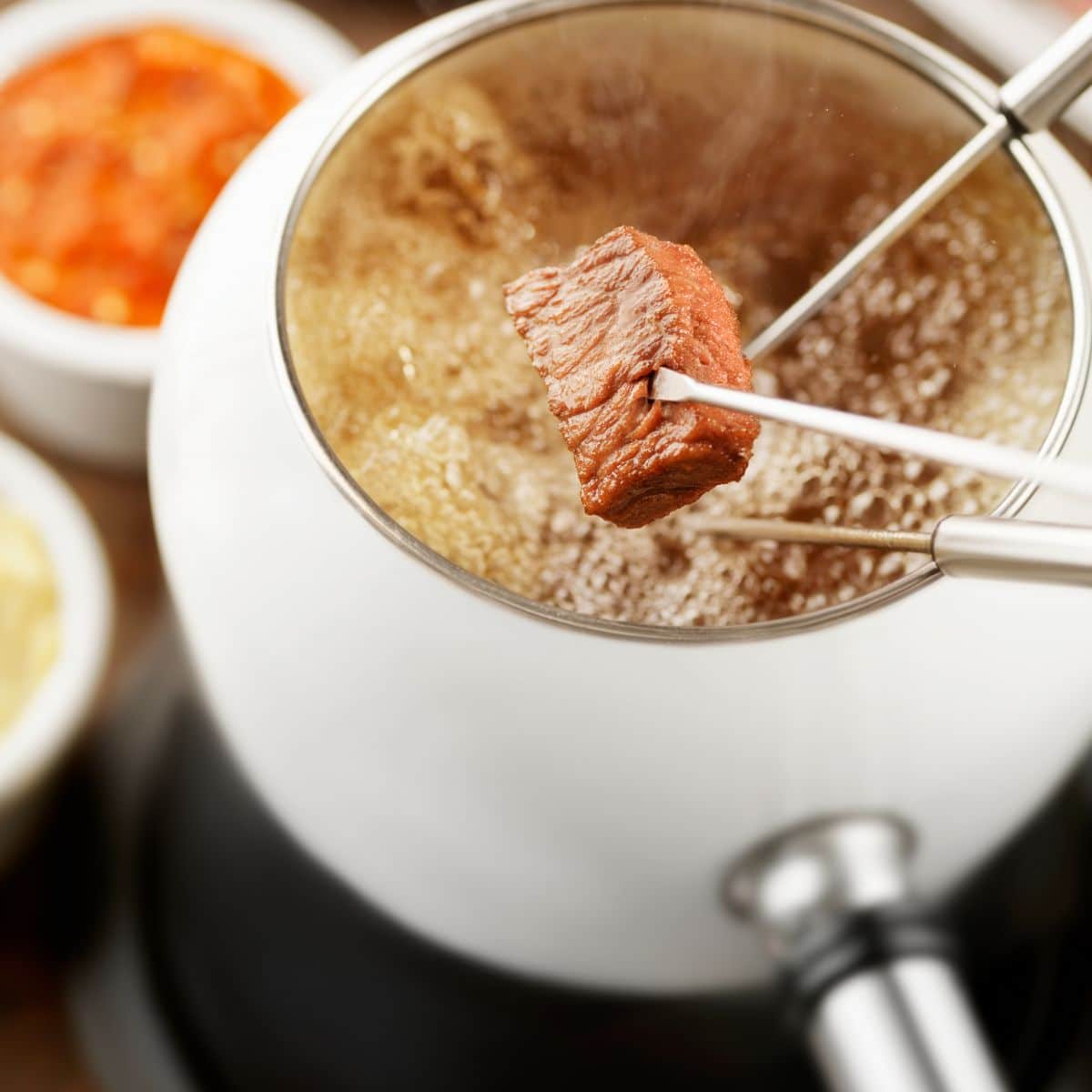 Square image of meat being dipped into oil fondue.